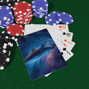 May include: A deck of playing cards with a whale illustration on the back, fanned out to reveal a ten of hearts, ten of spades, jack of diamonds, and jack of spades, surrounded by stacks of red, blue, and black poker chips on a green surface.