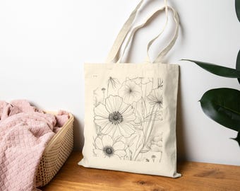 May include: A natural canvas tote bag featuring a black and white floral line drawing. The design includes detailed outlines of various flowers and foliage. The bag has sturdy handles and is suitable for carrying groceries or personal items.