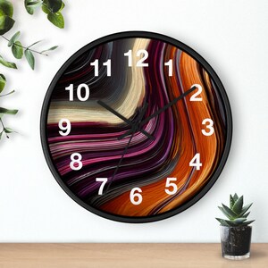 May include: A round wall clock with a black frame and a face featuring an abstract swirl pattern in shades of deep purple, burnt orange, cream, and charcoal gray. The clock has large white Arabic numerals and thin black hour, minute, and second hands.