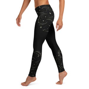 Könnte beinhalten: Schwarze Leggings mit einem himmlischen Design mit wirbelnden Mustern, Sternen und goldenen Monden. Die Leggings haben eine hohe Taille und eine figurbetonte Silhouette, geeignet für Yoga oder Freizeit.