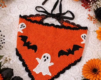 May include: A triangular crochet bandana in bright orange featuring a black scalloped border and black tie strings. The fabric displays white ghost motifs and black bat silhouettes distributed across the surface in a repeating pattern.