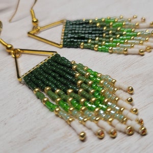 May include: A pair of green and white beaded earrings with gold triangle accents. The earrings are made with small seed beads and have a graduated ombre effect.