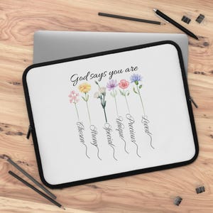 May include: White laptop sleeve with a black border featuring a floral design and the text "God says you are." The design includes watercolor flowers and the words "Chosen, Strong, Special, Unique, Precious, Loved."