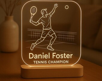 May include: A tennis-themed LED lamp featuring a player in action, with a racket and ball. The lamp has a wooden base and a clear acrylic panel with the name "Daniel Foster" and the text "TENNIS CHAMPION".