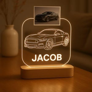 May include: A personalized LED night light featuring a car design and the name "JACOB" in white. The light has a wooden base and includes a small photo of a car at the top. The overall design is a warm, inviting glow.