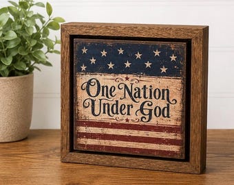 May include: A square wooden sign featuring a distressed American flag design with a blue field of white stars above red and white stripes. The text One Nation Under God is printed in black in the center of the sign, which is set in a brown frame.