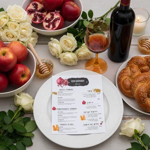 Può includere: Un'impostazione festosa della tavola per la cena del Rosh Hashanah. L'immagine presenta un piatto bianco con un menu, pane challah, mele, melograni, vino e rose bianche. È presente anche una piccola ciotola di miele con un mestolo.