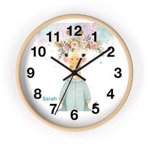 May include: A round wall clock with a light wood frame. The clock face features a watercolor illustration of a giraffe wearing a floral crown and a blue robe. The clock hands are black, and the numbers are black.