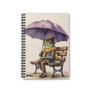 Puede incluir: Cuaderno de espiral con una ilustración en acuarela de una rana con sombrero y bufanda, sosteniendo un paraguas morado mientras está sentada en un banco del parque. La palabra "Relax" está impresa en la parte inferior izquierda.