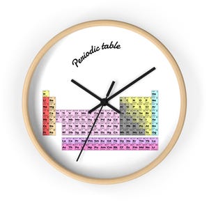 May include: A round wall clock with a light wood frame. The clock face is white and features a colorful periodic table of elements design. The words "Periodic table" are written in black script. Black clock hands indicate the time.