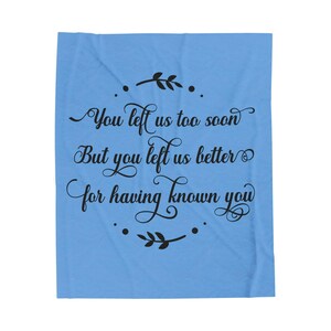 May include: A light blue blanket with black script that reads "You left us too soon But you left us better for having known you." The text is surrounded by decorative floral elements.