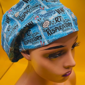 May include: A light blue medical scrub cap with a repeating pattern of respiratory-related words and phrases in white and black. The cap features words like "Vent," "Respiratory," and "Nebulizers." The cap is worn by a mannequin.