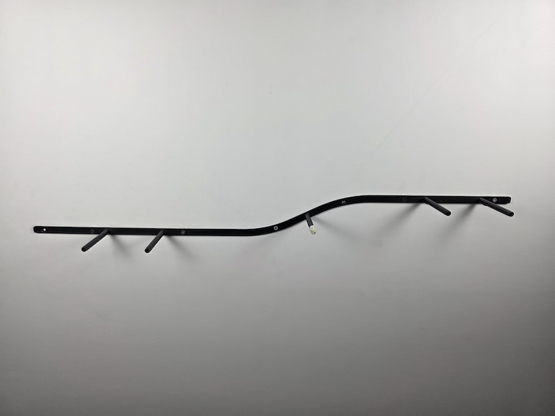 K&ouml;nnte beinhalten: Eine schwarze Klimmzugstange zur Wandmontage mit mehreren abgewinkelten Griffen. Die Stange hat ein gebogenes Design und ist an einer wei&szlig;en Wand befestigt. F&uuml;r das Oberk&ouml;rpertraining.