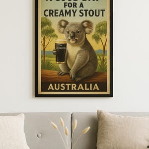 May include: Poster featuring a koala holding a pint of Guinness stout. The poster has the text "A Good Day for a Creamy Stout" and "Australia". The koala is sitting on a log with trees in the background. The poster is framed in black.