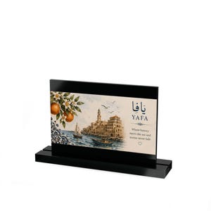 May include: A rectangular acrylic plaque on a black stand featuring a watercolor illustration of the Yafa coastline with orange trees, boats, and buildings. The text reads Yafa, in Arabic and English, with the phrase Where history meets the sea.