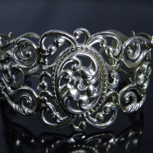 Puede incluir: Pulsera de filigrana de plata con un diseño floral detallado. La pulsera está hecha de intrincados remolinos y bucles, creando un aspecto delicado y elegante.