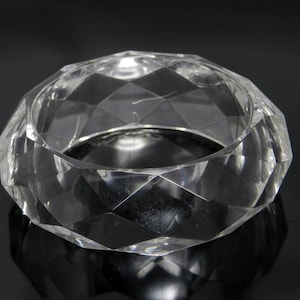 May include: A clear, faceted, plastic bangle bracelet. The bracelet is made of a hard, durable plastic and has a smooth, polished finish.