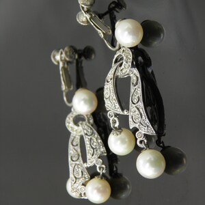 May include: A pair of silver tone clip-on earrings with a delicate, ornate design and three white pearls dangling from each earring.