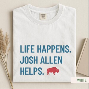 May include: White t-shirt with the text "LIFE HAPPENS. JOSH ALLEN HELPS." in blue, and a red buffalo graphic. The shirt is made of a soft material and has a crew neck.