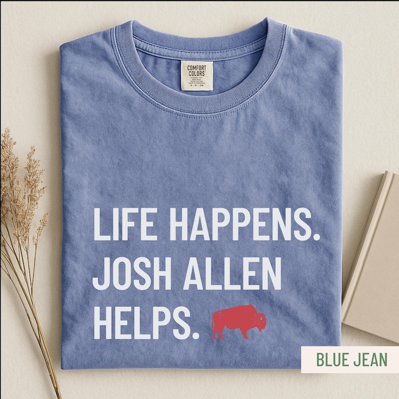 May include: Blue jean colored t-shirt with the text "LIFE HAPPENS. JOSH ALLEN HELPS." in white. A red buffalo graphic is below the text. The shirt has a crew neck and a Comfort Colors tag.