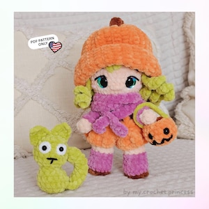May include: A crochet doll wearing an orange pumpkin hat, a purple scarf, and matching purple leg warmers, holding a small orange jack-o'-lantern bucket. Beside it sits a small, light green crochet cat. Text reads: PDF PATTERN ONLY.