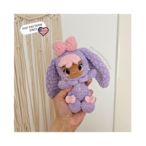 Könnte beinhalten: Eine handgefertigte Plüsch-Hasenpuppe in Lila- und Rosatönen. Die Puppe hat eine große rosa Schleife, ein blütenförmiges Gesicht und herzförmige Füße. Der Text "PDF PATTERN ONLY" ist oben links sichtbar. Die Puppe wird in einer Hand gehalten.