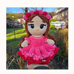 Könnte beinhalten: Handgefertigte Häkelpuppe mit rosa Kleid und Blumenstirnband. Die Puppe hat braune Haare, blaue Augen und einen hellen Hautton. Der Text "PDF PATTERN ONLY" ist im Bild zu sehen.