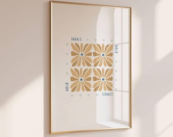 May include: Framed art print with a gold frame. The artwork features four stylized tan flowers with blue centers, arranged in a square. The words "INHALE," "HOLD," and "EXHALE" are written in blue. Small blue circles surround the flowers.