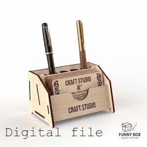 以下が含まれることがあります： CRAFT STUDIOの文字と糸巻きのアイコンが刻印された名刺用スロットと、黒と金のペンを収納する2つの円形の穴を備えた、明るい色の木製デスクオーガナイザー。前面パネルにもCRAFT STUDIOの文字が刻印されています。