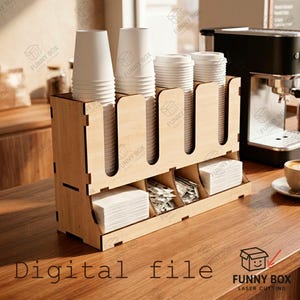 May include: A light-colored wooden coffee station organizer featuring four vertical slots for stacking disposable cups and three lower compartments for storing napkins and stirrers. The unit has a modular design with visible joints.