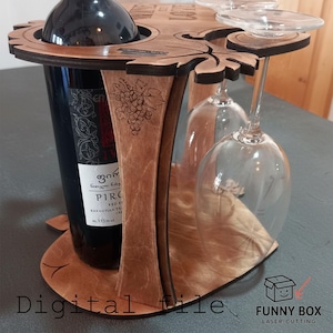 May include: Wooden wine bottle and glass holder. The holder is made of light brown wood and features a circular design with space for a wine bottle and two wine glasses. The design includes leaf and grape details.