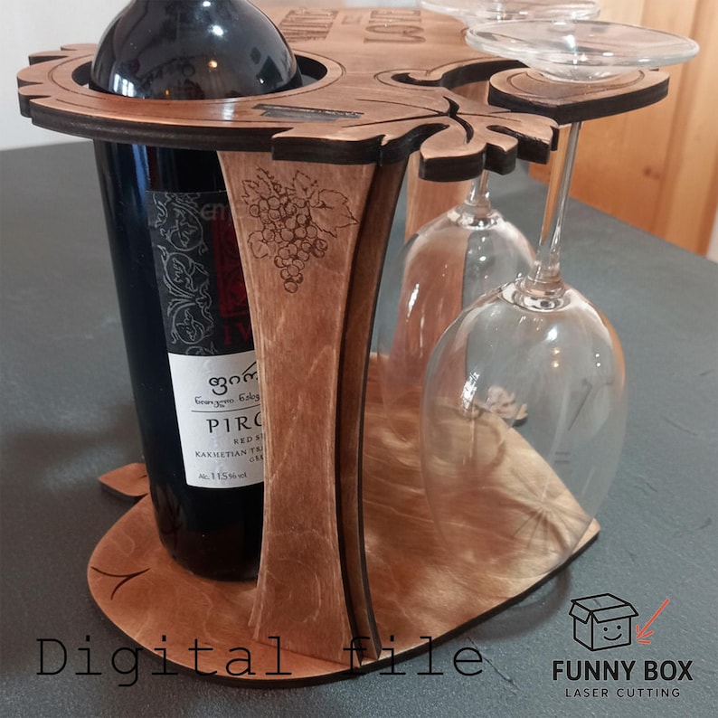 May include: Wooden wine bottle and glass holder. The holder is made of light brown wood and features a circular design with space for a wine bottle and two wine glasses. The design includes leaf and grape details.