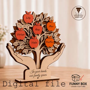 Peut inclure: Un arbre généalogique en bois découpé au laser. L'arbre comporte six pommes avec des noms. La base porte l'inscription "In your hands our family grows" et "Digital file".