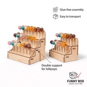 Può includere: Due espositori in legno a gradini per lecca-lecca e cake pops. Le strutture in legno chiaro presentano diverse file di fori per sostenere i dolci. Il testo indica montaggio senza colla, facile trasporto e doppio supporto per lecca-lecca. Il marchio Funny Box Laser Cutting è visibile nell'angolo.