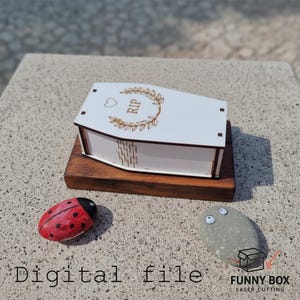 May include: A white, coffin-shaped wooden box with the letters "RIP" and a heart and wreath design. The box sits on a dark wooden base, with a painted ladybug and a stone with googly eyes nearby. The words "Digital file" are at the bottom.