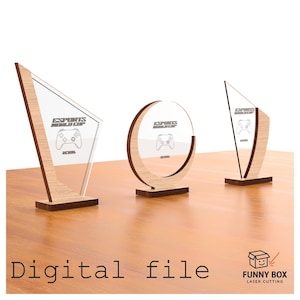 Op de afbeelding: Drie trofeeën van hout en helder acryl met de tekst "ESPORTS WORLD CUP" en een gamecontroller-afbeelding. De trofeeën hebben verschillende vormen: een driehoek, een cirkel en een trapezium. De tekst "Digital file" staat onderaan.