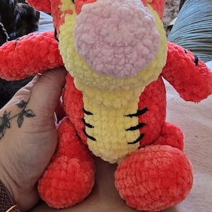 Puede incluir: Un peluche de tigre naranja y amarillo con una nariz rosa y rayas negras. El peluche tiene un aspecto suave y texturizado y probablemente est&aacute; hecho a mano. El juguete es un art&iacute;culo para ni&ntilde;os.