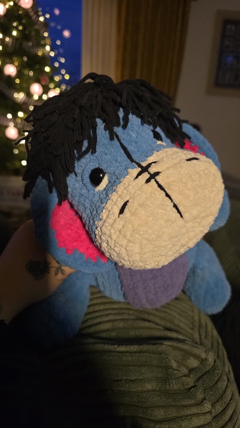 Puede incluir: Un peluche de Eeyore, el burro de Winnie the Pooh, en tonos azules, rosas y morados. El juguete tiene pelo de hilo negro y un hocico color crema. El juguete es suave y tierno.
