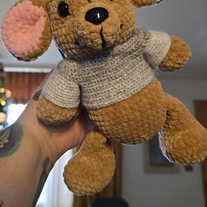 Puede incluir: Un juguete de peluche hecho a mano con forma de oso. El oso es marr&oacute;n con el interior de las orejas rosa y un su&eacute;ter gris. Tiene ojos negros y una nariz negra. El juguete es suave y tierno.
