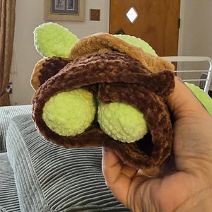 Puede incluir: Un juguete de taco de ganchillo hecho a mano con dos mitades de aguacate verdes. La concha del taco es marr&oacute;n y el aguacate es verde brillante. El juguete es suave y afelpado, para ni&ntilde;os.