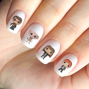 Op de afbeelding: Vier witte vingernagels met Harry Potter-personage nagelstickers. De stickers tonen Harry Potter, Dobby, Hermelien Griffel en Ron Wemel.