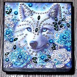 May include: Square artwork featuring a wolf's face with piercing blue eyes. The image is embellished with sparkling rhinestones and teal-colored gems, creating a shimmering effect. The background has a light blue floral design.