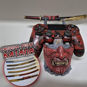 Könnte beinhalten: Ein rot-schwarzer PlayStation 4-Controller mit einem Katana-Schwert oben. Der Controller ruht auf einer roten Oni-Maskenbasis. Das Bild enthält eine Grafik mit der Aufschrift "Wähle dein Katana" und zeigt mehrere Katana-Designs.