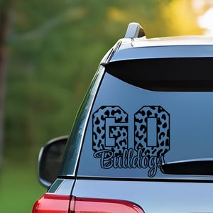 May include: Black decal on a car window. The decal says "GO Bulldogs" in a stylized font. The letters "GO" are filled with a black and white animal print pattern. The word "Bulldogs" is in a cursive font.