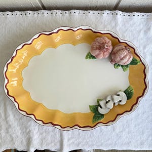 Puede incluir: Plato ovalado para servir con un borde amarillo festoneado y un centro blanco. El plato de cerámica está decorado con acentos de ajo y champiñones. El borde está adornado con un borde rojo oscuro.