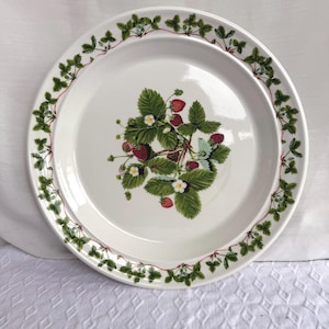 Puede incluir: Plato de cerámica blanco con diseño de fresas. El plato presenta un grupo central de fresas, hojas verdes y flores blancas. Un borde de hojas y vides verdes rodea el borde del plato.