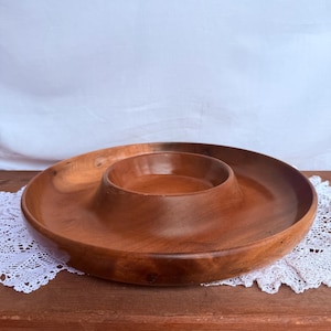 Könnte beinhalten: Eine Holzschale zum Servieren von Chips und Dips. Die Schale besteht aus warm getöntem Holz und hat ein kreisförmiges Design mit einem erhöhten Mittelteil für den Dip. Die Schale steht auf einer Holzoberfläche.