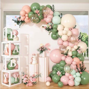 Può includere: Decorazione per baby shower con arco di palloncini rosa, verdi e crema. L'arco è decorato con fiori e palloncini pieni di coriandoli. Scatole bianche con la scritta "BABY" con palloncini all'interno. Include una torta e composizioni floreali.