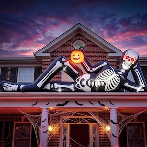 May include: A large inflatable skeleton decoration lying on a roof, featuring black fabric with white bone patterns, glowing red eyes, and a bright orange jack-o'-lantern held in one hand, positioned against a sunset sky background.