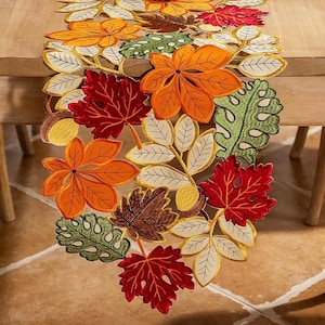 May include: A table runner featuring an intricate embroidered pattern of autumn leaves in shades of orange, red, brown, and green. The design includes detailed stitching on maple and oak-style foliage, interspersed with small yellow acorn motifs.